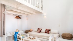 A white room with a sofa, a table, chairs, a hanging rack, and a ceiling with a railing. - Atlantis Houses (Halki)