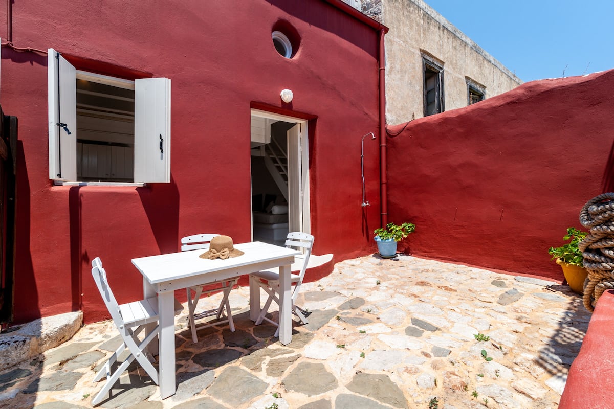 Um edifício pintado de vermelho com piso de pedra, uma mesa branca com cadeiras e um vaso de planta.