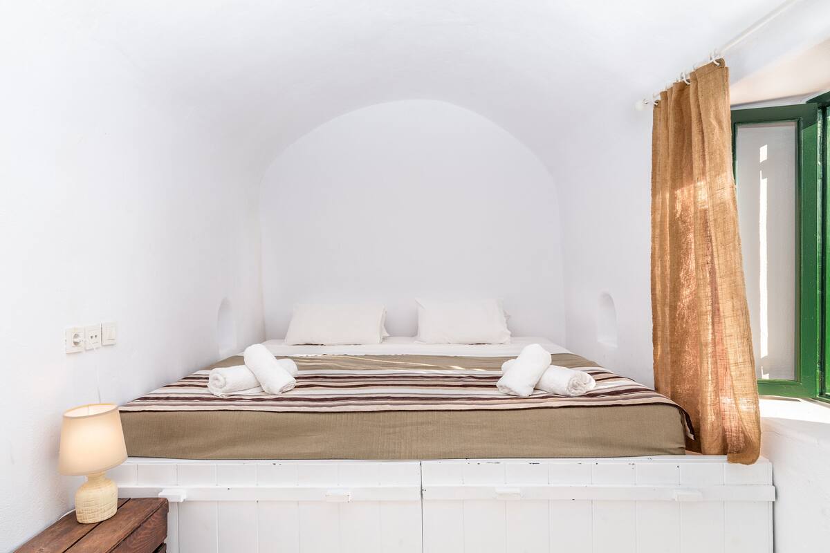 Uma cama bem arrumada com um cobertor listrado, almofadas brancas e duas toalhas dobradas ao pé da cama.