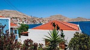A coastal town with terracotta-roofed buildings, a clear blue sky, and a mountainous backdrop. - Atlantis Houses (Halki)