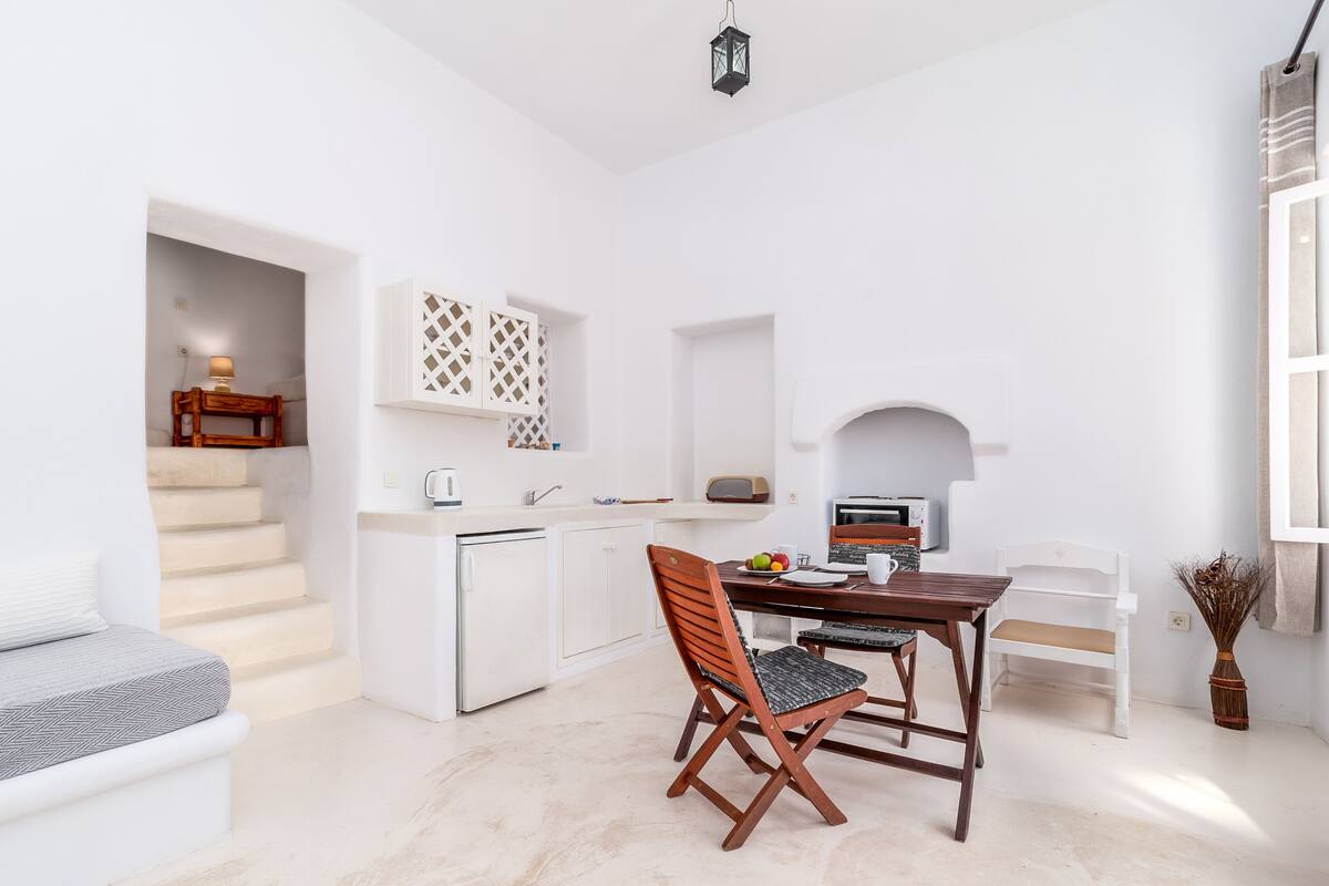 Espaço compacto com cozinha compacta, área de jantar com mesa e cadeiras, sofá e escada que leva a um andar superior.