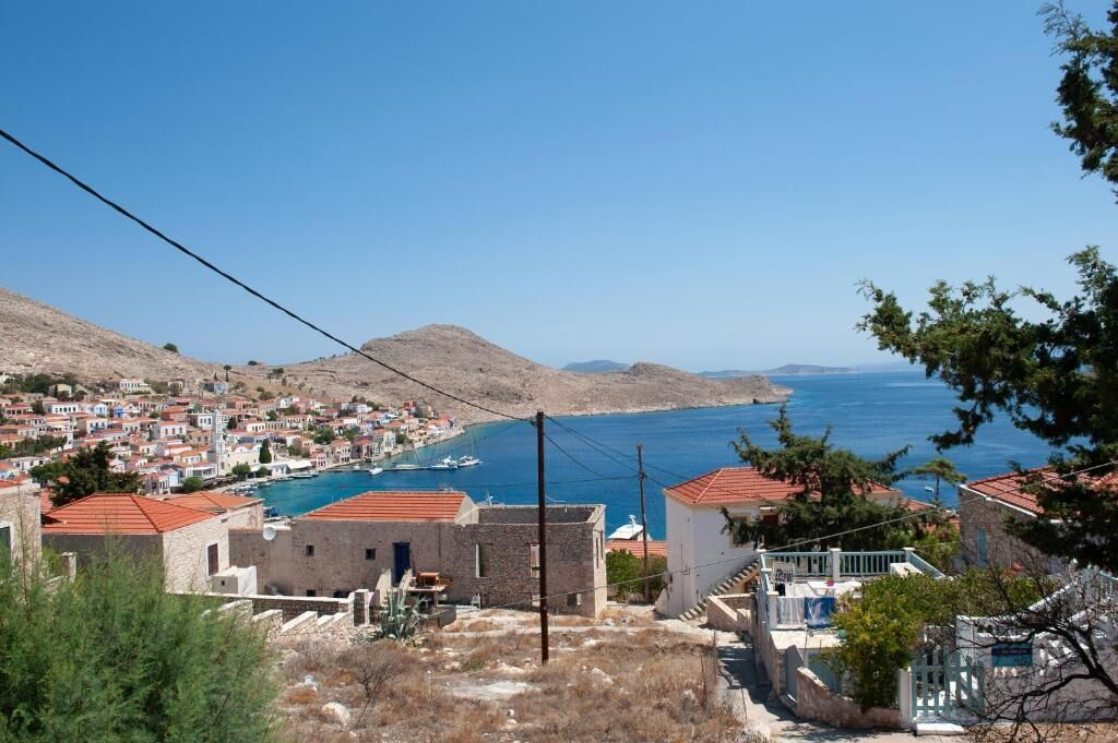Un pueblo costero con edificios, mar azul cristalino y colinas al fondo.