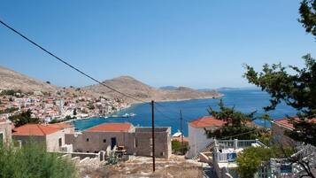 Un pueblo costero con edificios, mar azul cristalino y colinas al fondo.