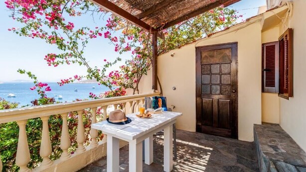 A balcony with a table, a hat, and a drink, overlooking the sea with boats. - Atlantis Houses (Halki)