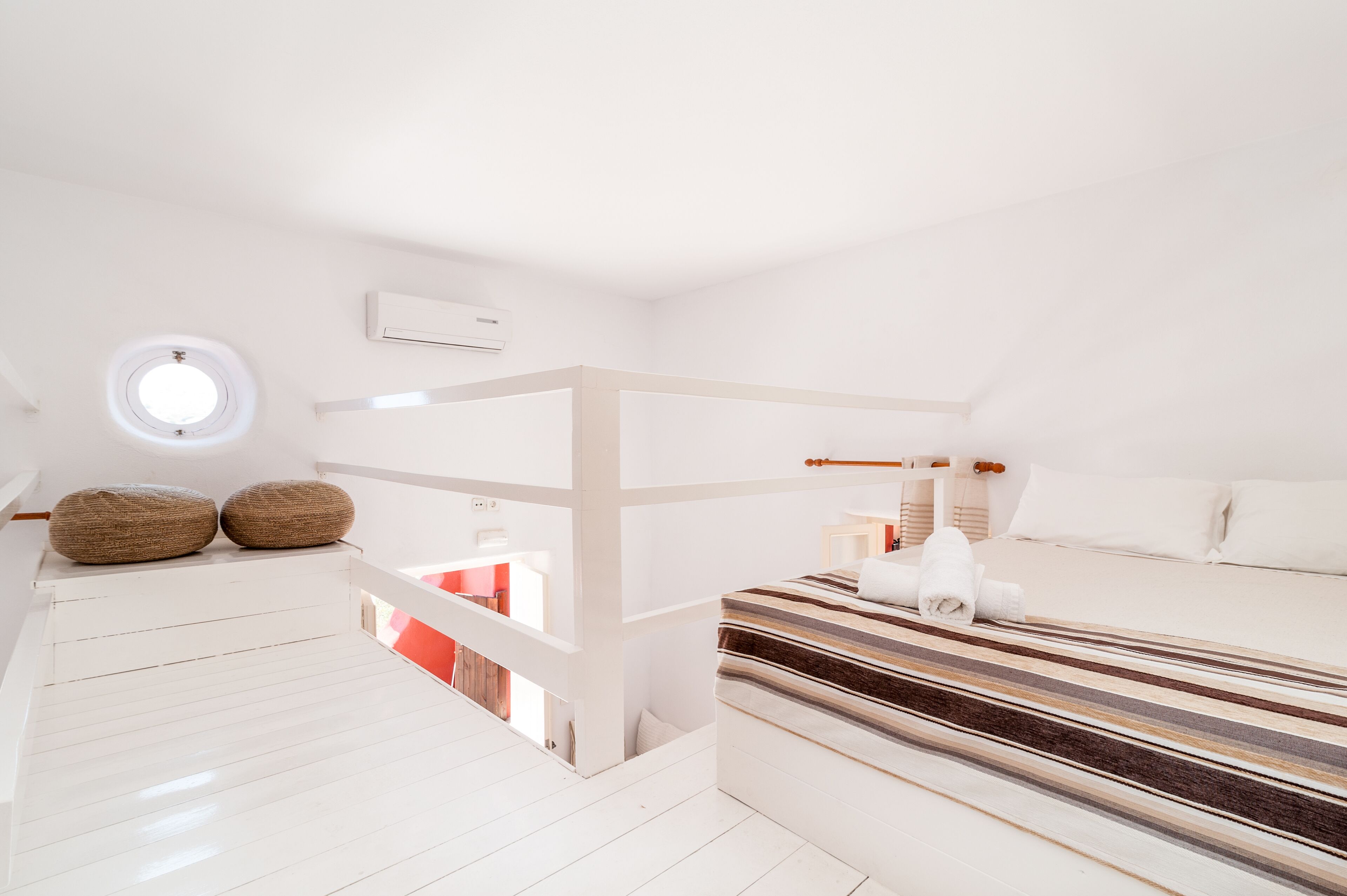Une chambre à coucher moderne, aux tons blancs, avec un lit superposé, une lucarne circulaire et une couvre-lit à rayures.