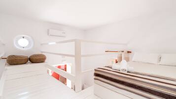 Une chambre à coucher moderne, aux tons blancs, avec un lit superposé, une lucarne circulaire et une couvre-lit à rayures.