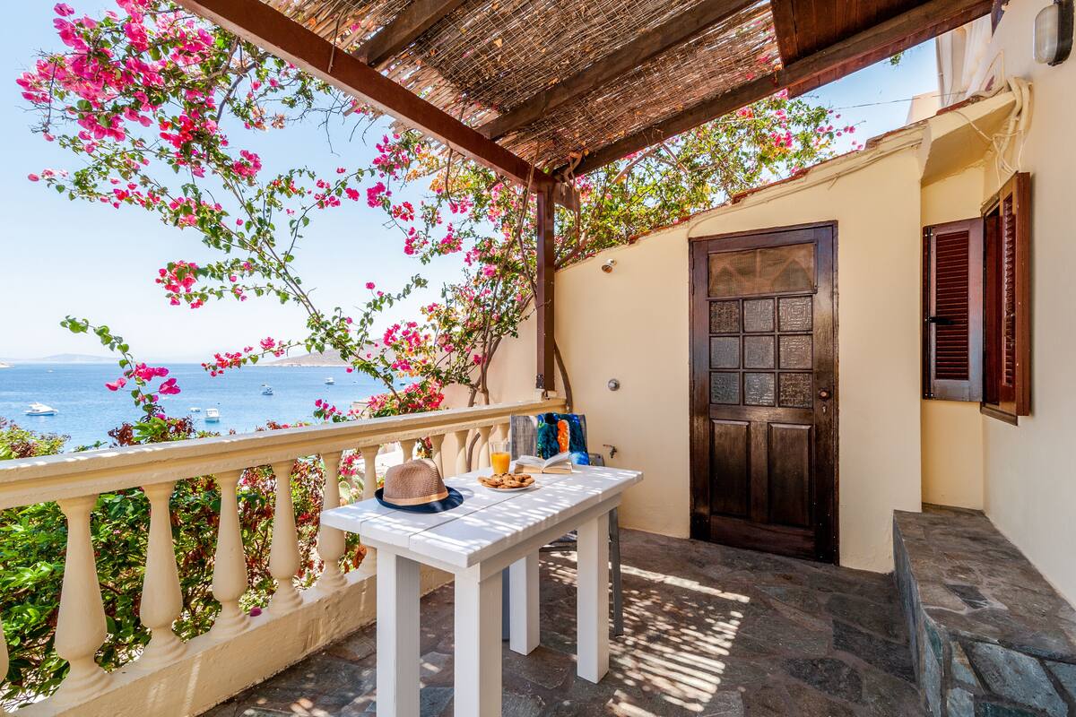 Uma varanda com mesa, porta e vista para o mar.