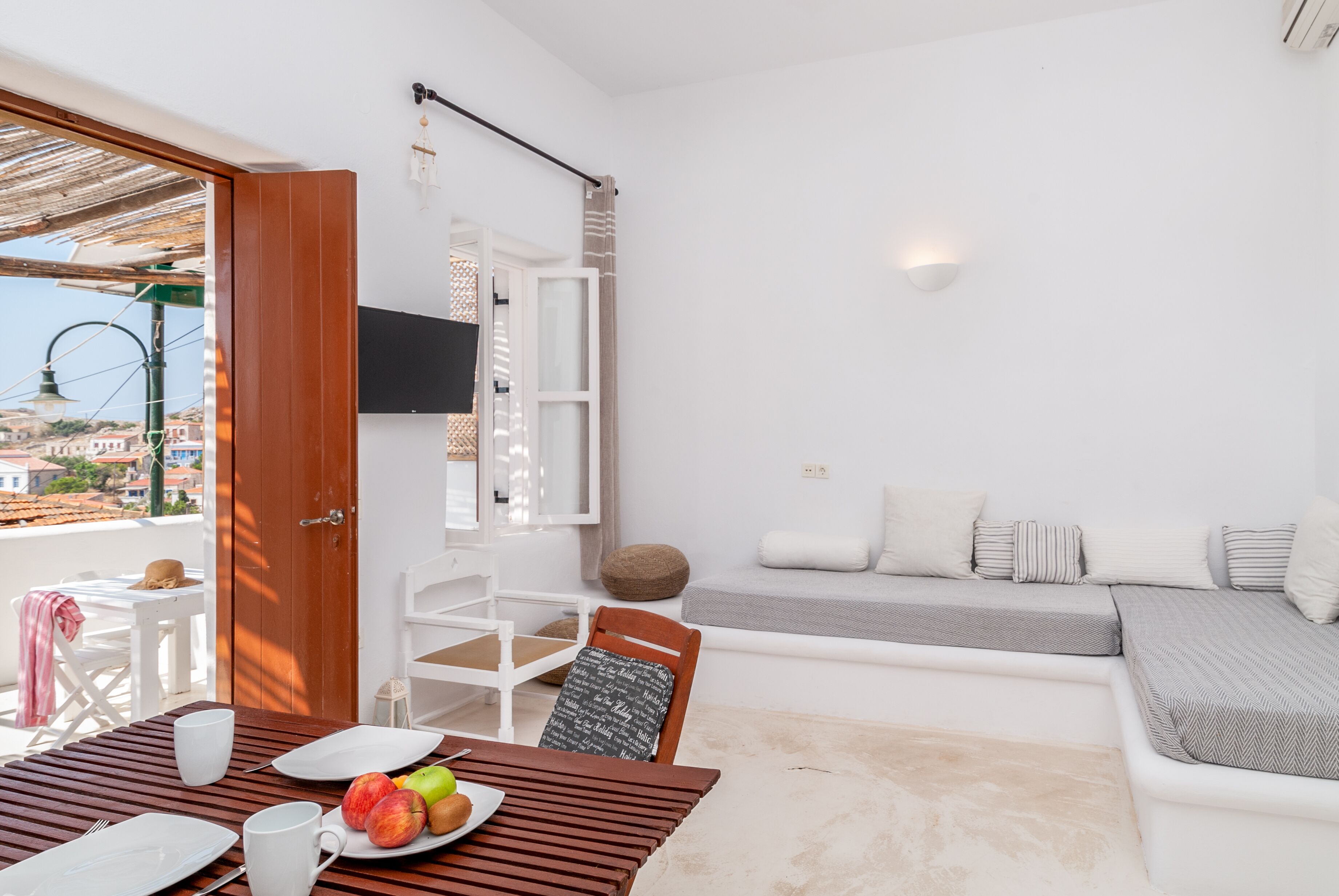 A modern, well-lit room with a dining area, a sofa, and a TV mounted on the wall.