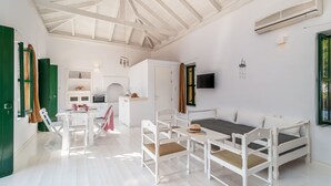 A spacious room with a high ceiling, a bed, a dining table with chairs, a kitchen area, and a TV mounted on the wall. - Atlantis Houses (Halki)