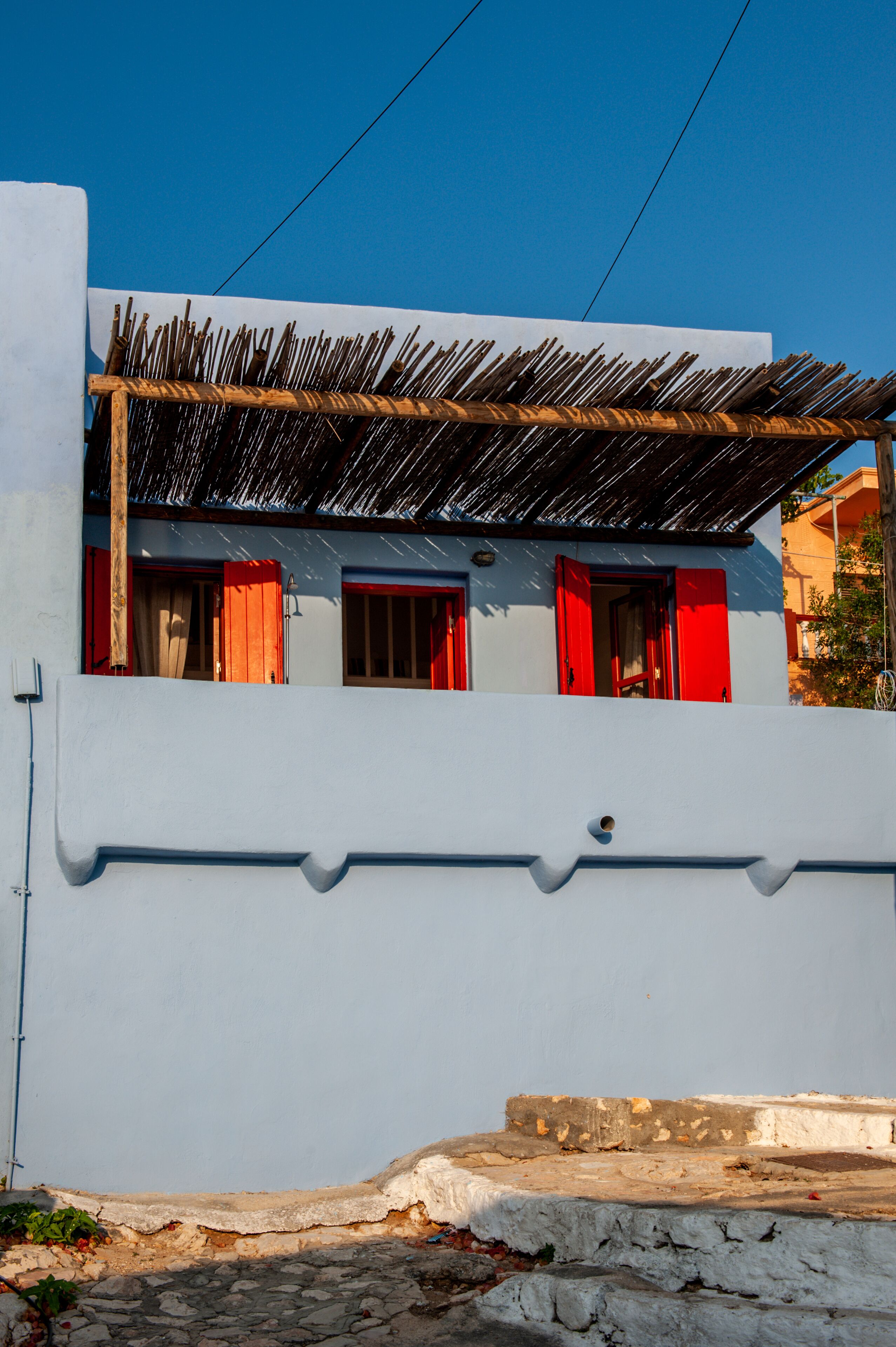 A building with a white exterior, red shutters, and a wooden pergola.