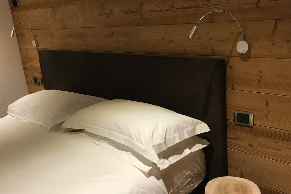 Een bed met witte beddengoed in een kamer met houten lambrisering.
