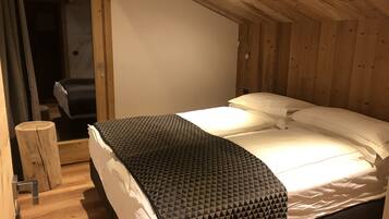 A single bed with a geometric-patterned blanket, a white pillow, and a wooden headboard in a room with wooden walls and a sloped ceiling.