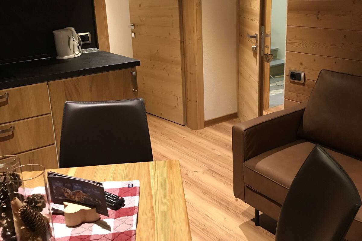 Een moderne keuken met een magnetron, waterkoker en een houten eettafel met stoelen.