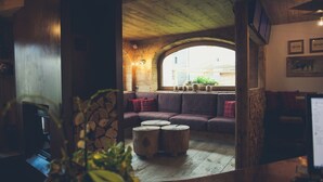 Ein gemütliches Interieur mit Holzbalkendecke, Steinwand, Couch aus Holz und einem kleinen Holztisch.