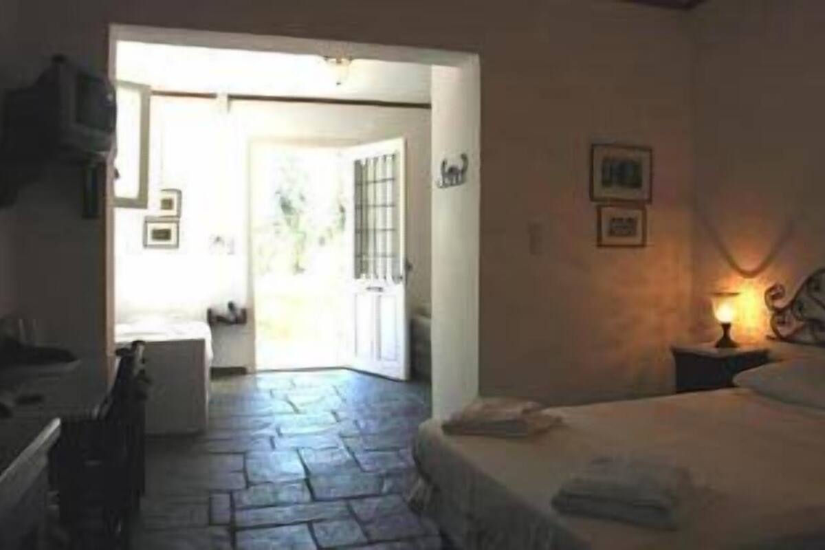 A bedroom with a bed, a nightstand with a lamp, a dresser, and a door leading to a bathroom.