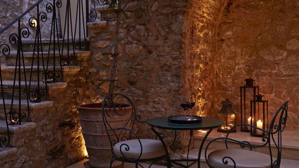 Una escalera de piedra con barandillas de hierro forjado, una mesa redonda con sillas y velas.