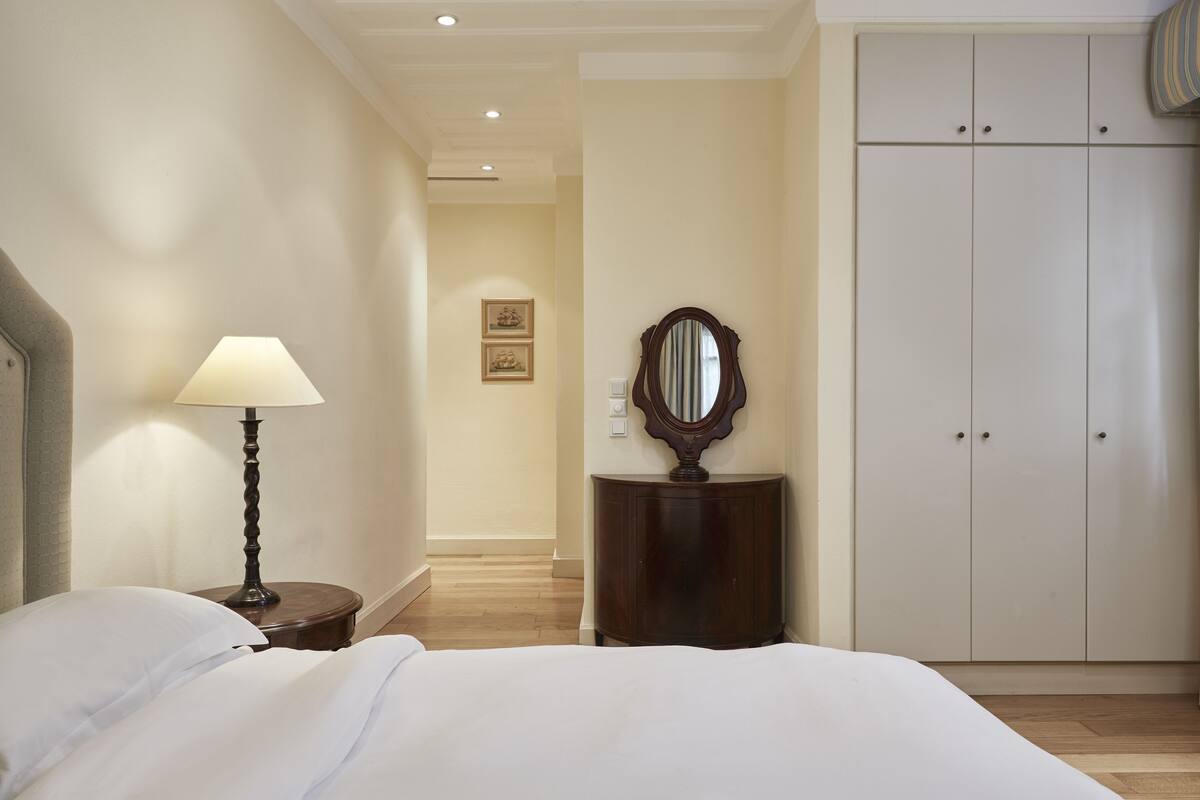 A hotel room with a bed, a bedside lamp, a mirror, a small wooden cabinet, and a wardrobe.