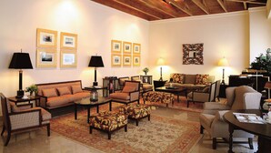 Un salón espacioso con techo alto, vigas de madera, un amplio sofá, varios sillones, una mesa de centro y una alfombra estampada.