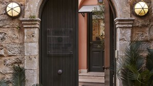 Un arco de piedra que da acceso a la entrada de un hotel, con una puerta de madera oscura, plantas en macetas y una lámpara sobre la puerta.