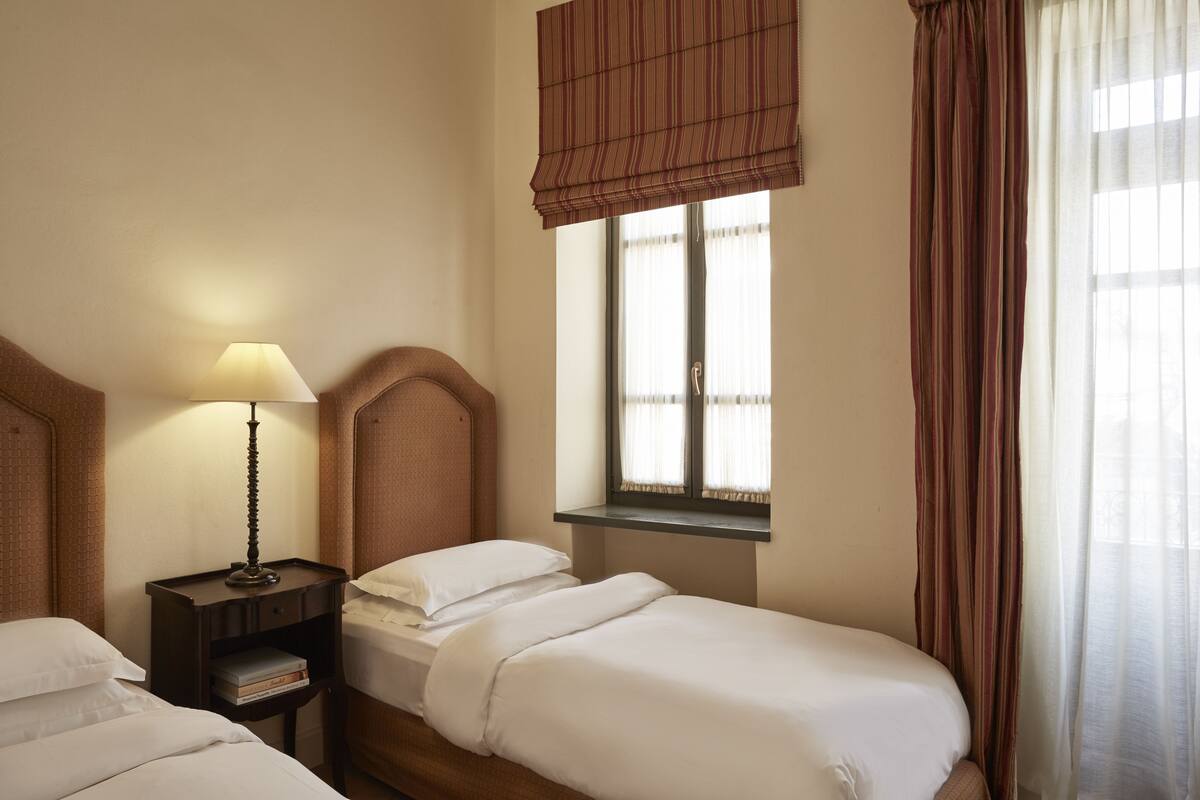 A hotel room with a bed, bedside table, lamp, and window with curtains.