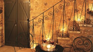 Una escalera de piedra con barandilla de hierro forjado, una puerta de madera y dos sillas con cojines.