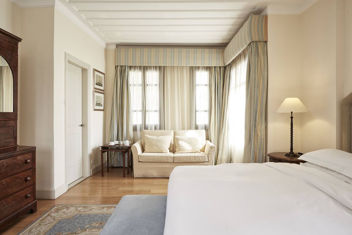 A bedroom with a bed, a nightstand, a dresser, and a window with curtains.