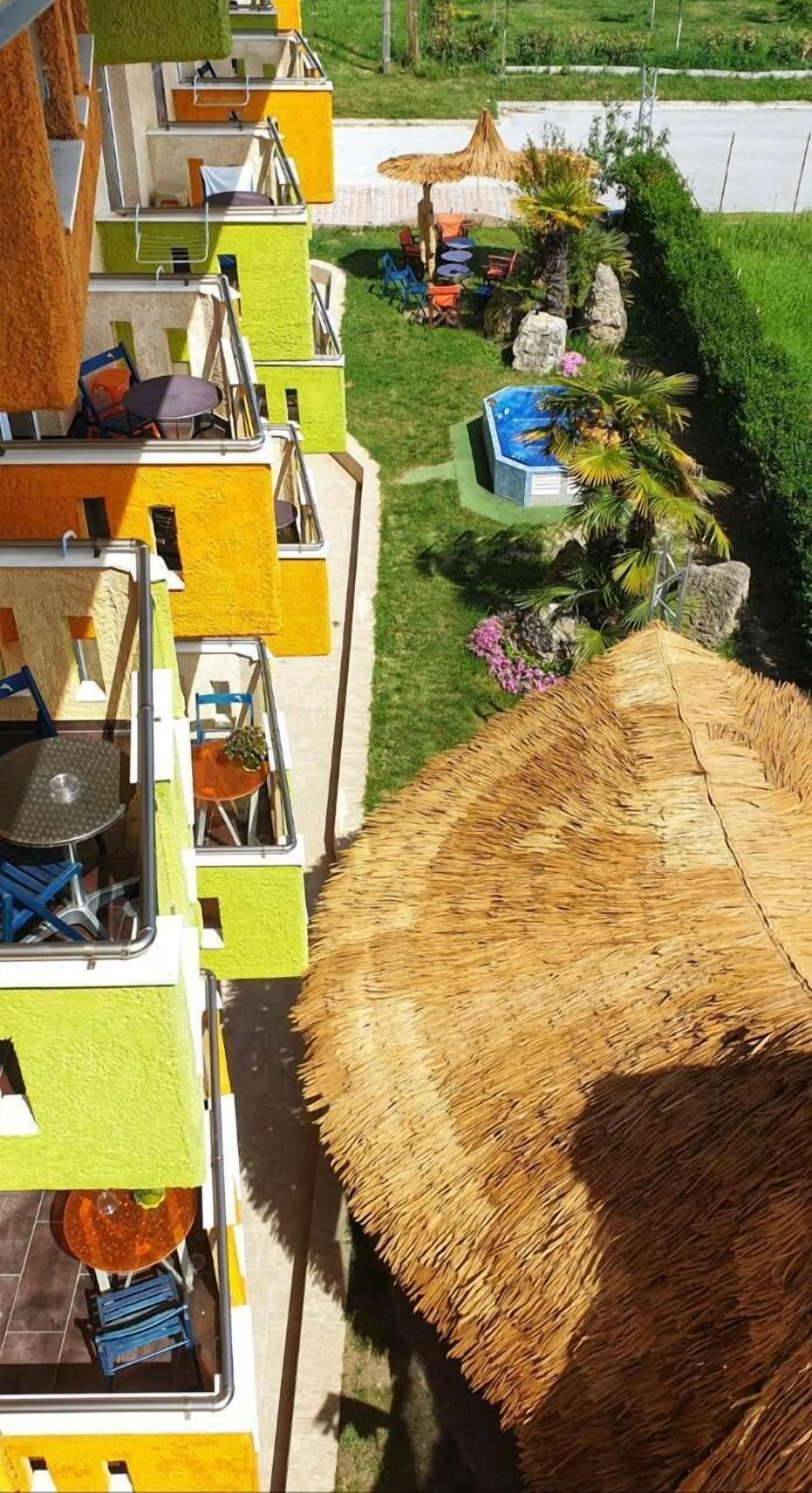 A hotel with multiple balconies, a thatched-roof outdoor area, and a swimming pool.
