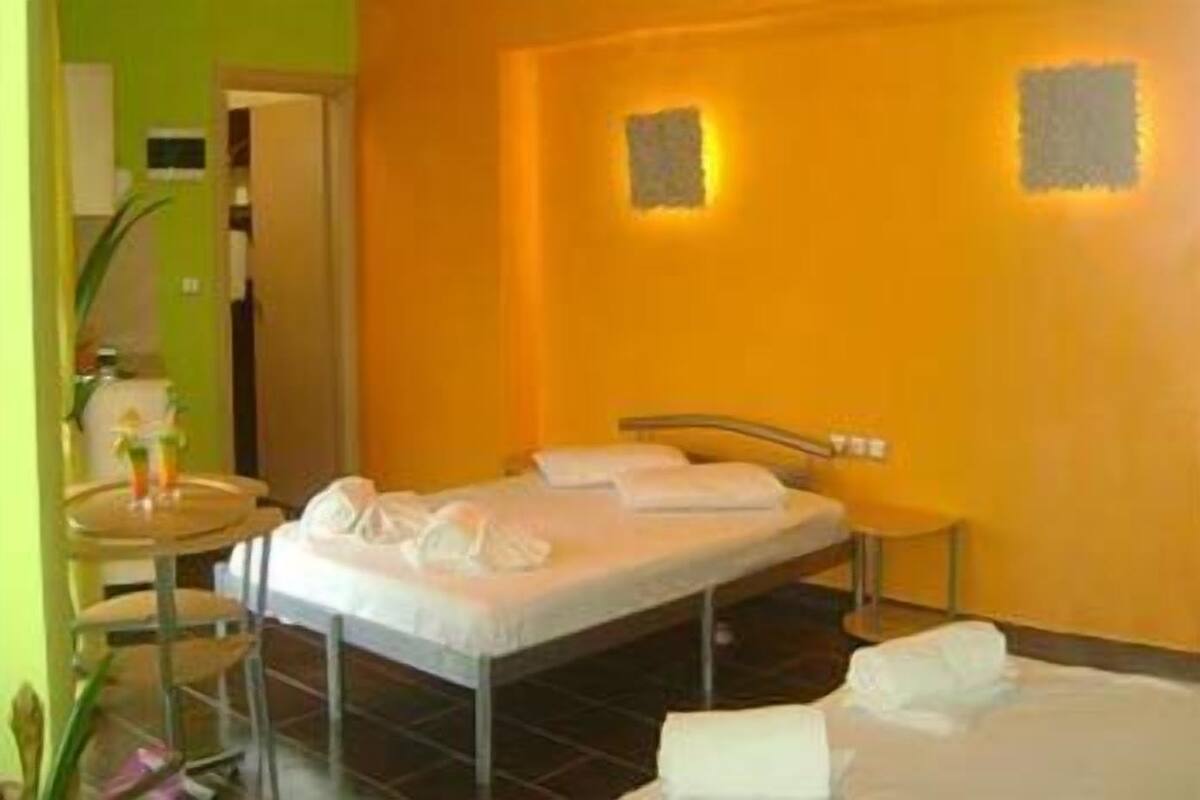 A hotel room with a bed, a bedside table, and a small table with a drink and a flower.