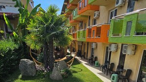 Une piscine dont le bord est recouvert de carreaux, entourée d’une pelouse bien entretenue et agrément ée d’un hamac.