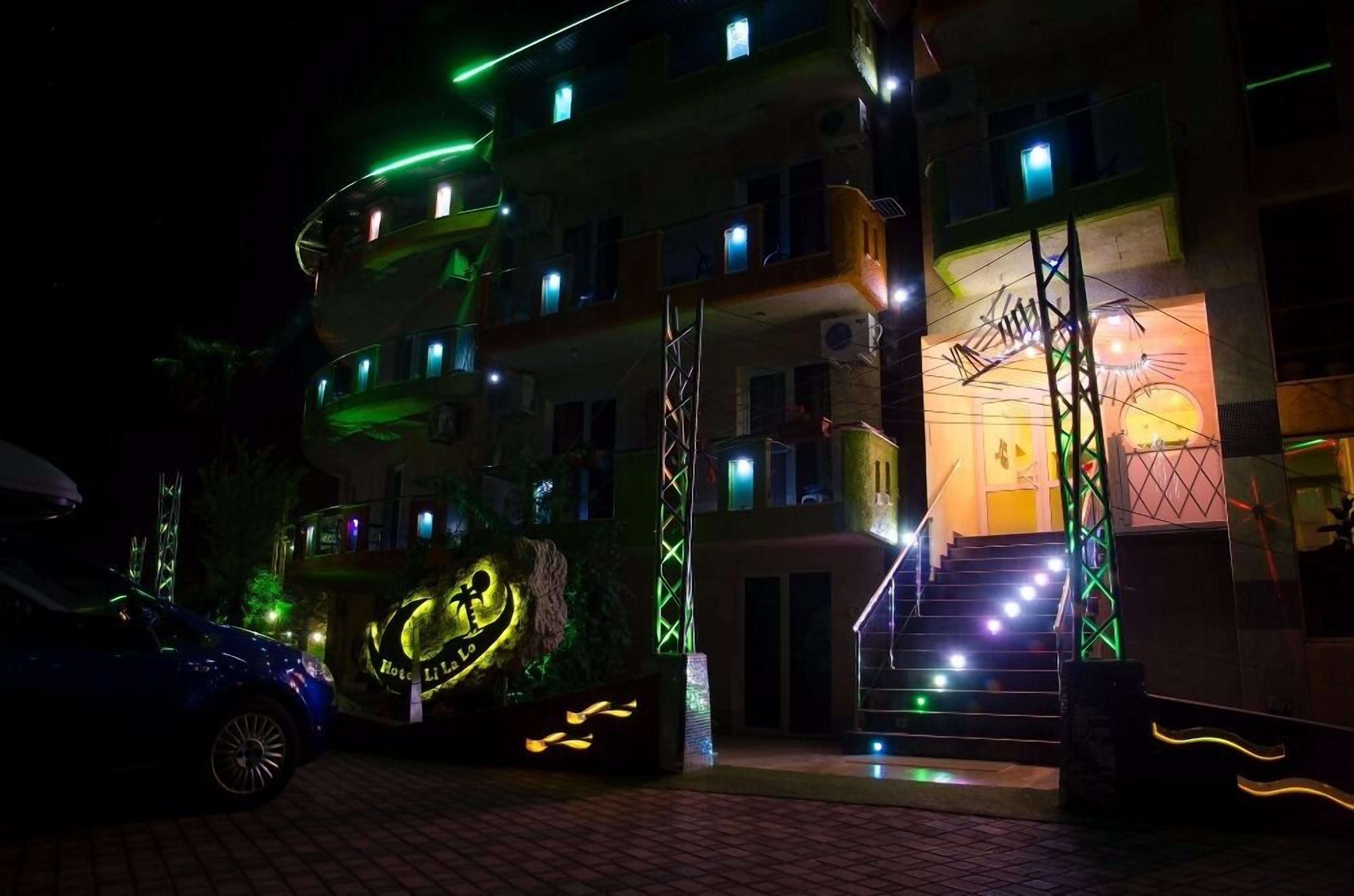 A multi-story building with balconies, a staircase, and a car parked in front.