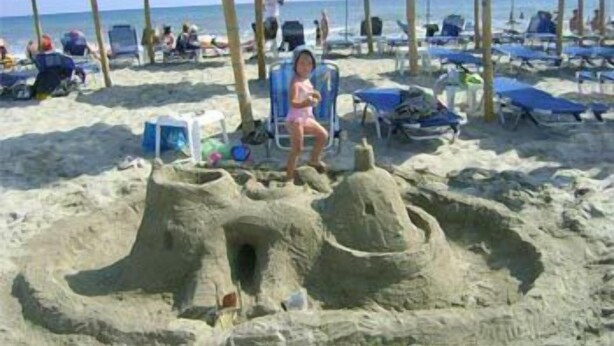 Une scène de plage avec un château de sable, des chaises de plage, des parasols et des personnes qui se détendent.