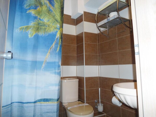 Un baño con cortina de ducha que muestra una escena de playa, un inodoro, un lavamanos y un estante con artículos de tocador.