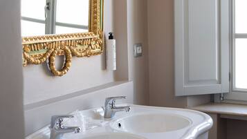 A bathroom with a double sink, a gold-framed mirror, and a window with a view.