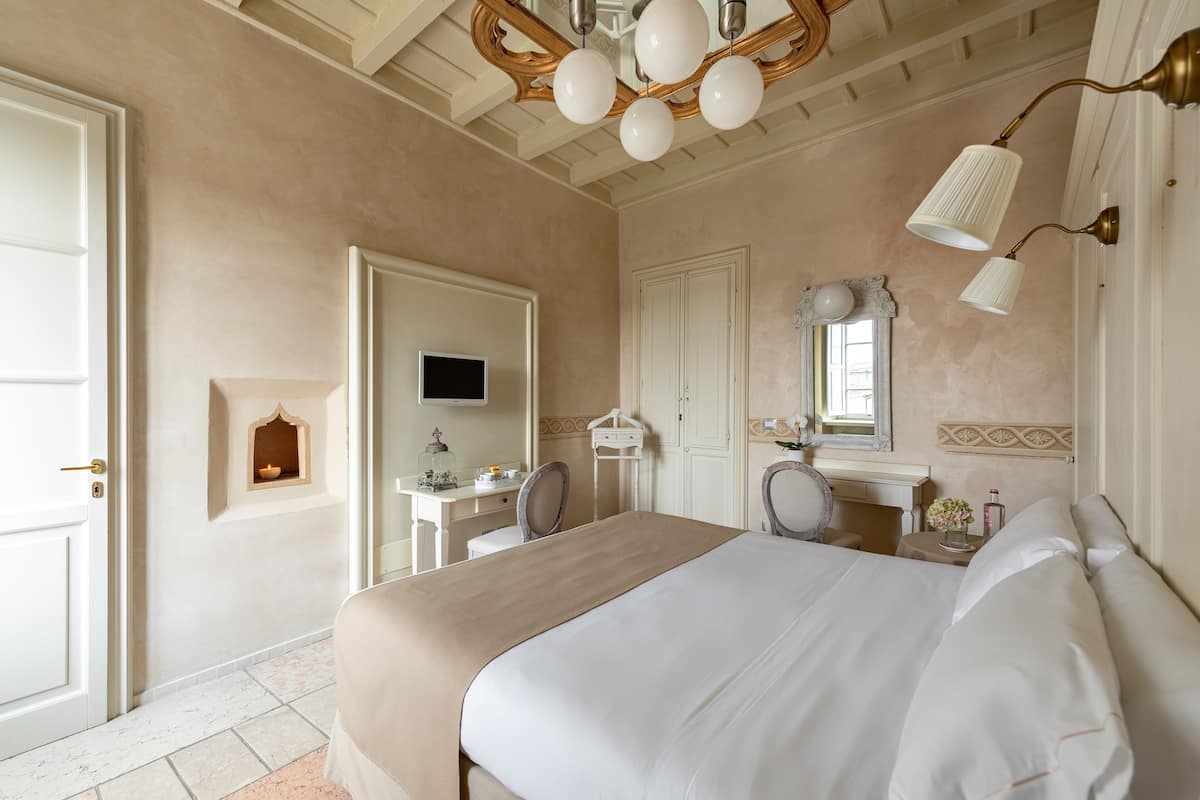 A hotel room with a large bed, a desk with a chair, a television, and a mirror.