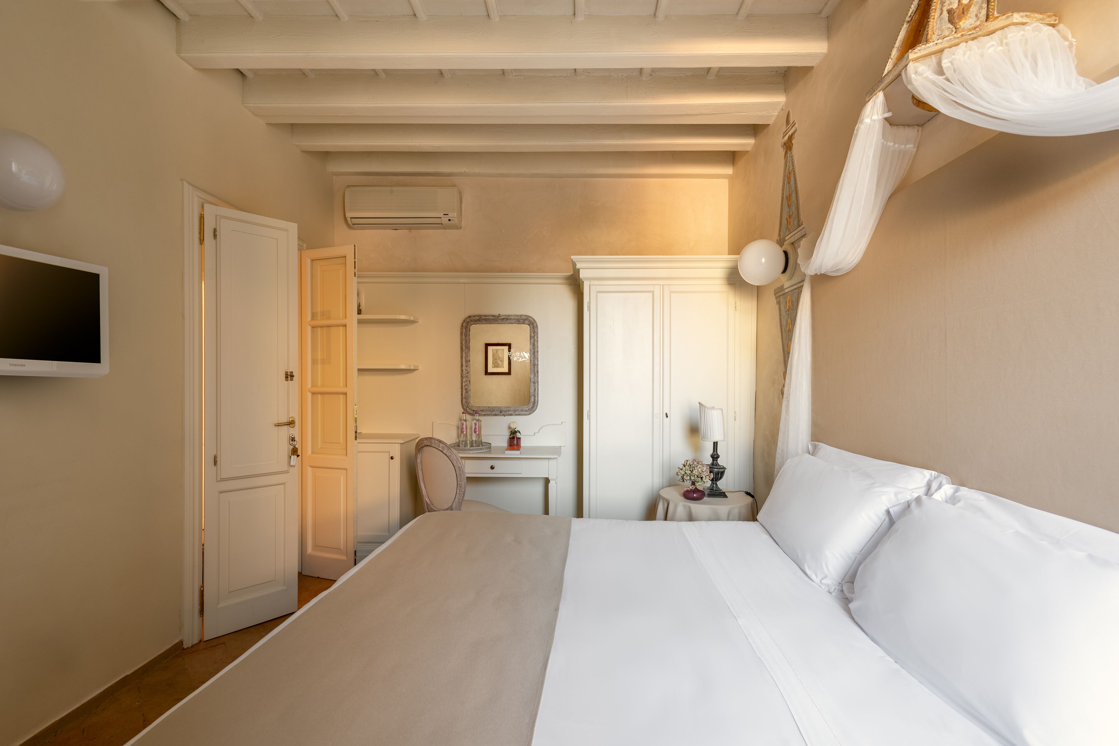 Un dormitorio con una cama, un escritorio, una silla, un televisor y un espejo.