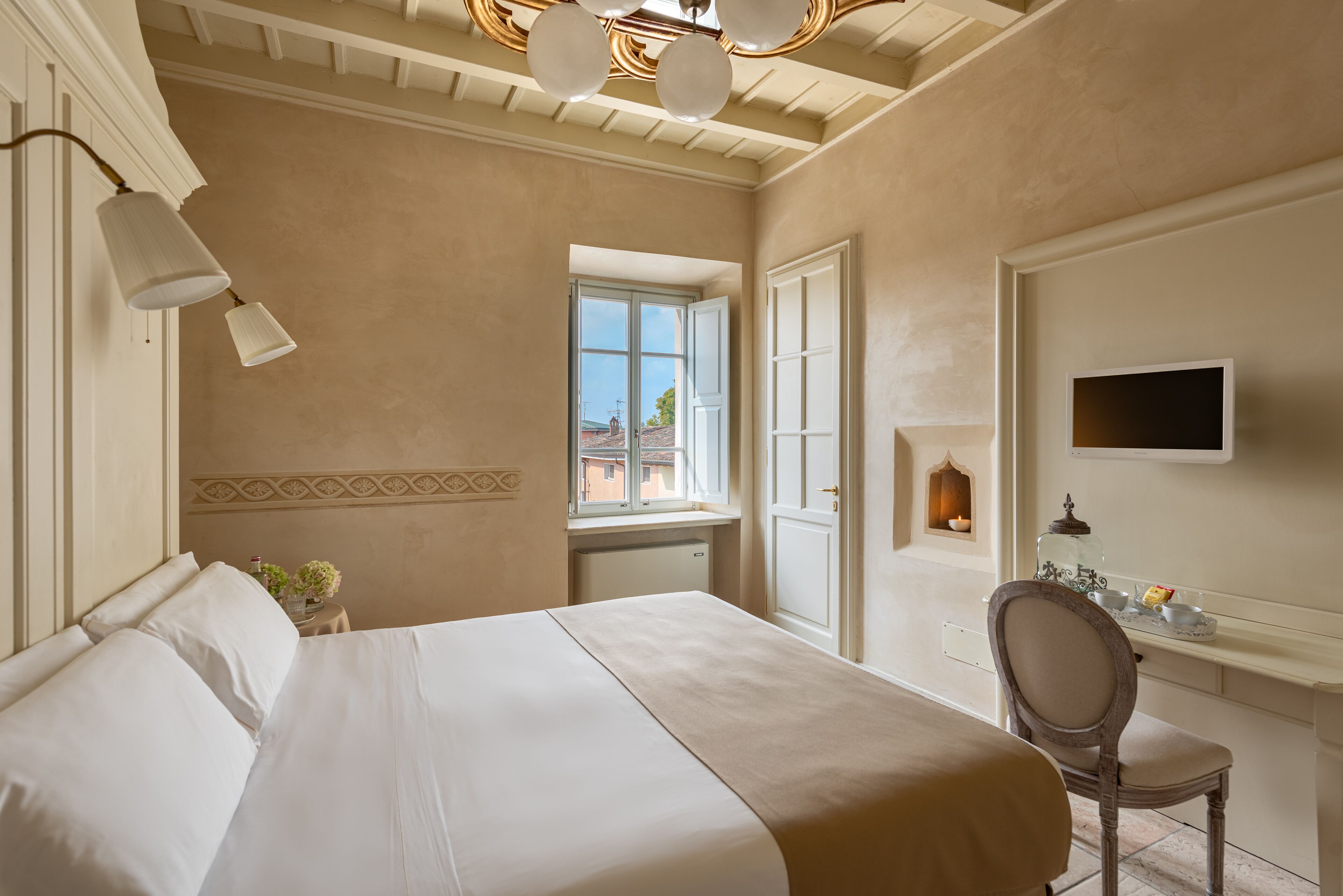 Habitación de hotel con cama, escritorio, silla, televisor y ventana con vista a edificios.