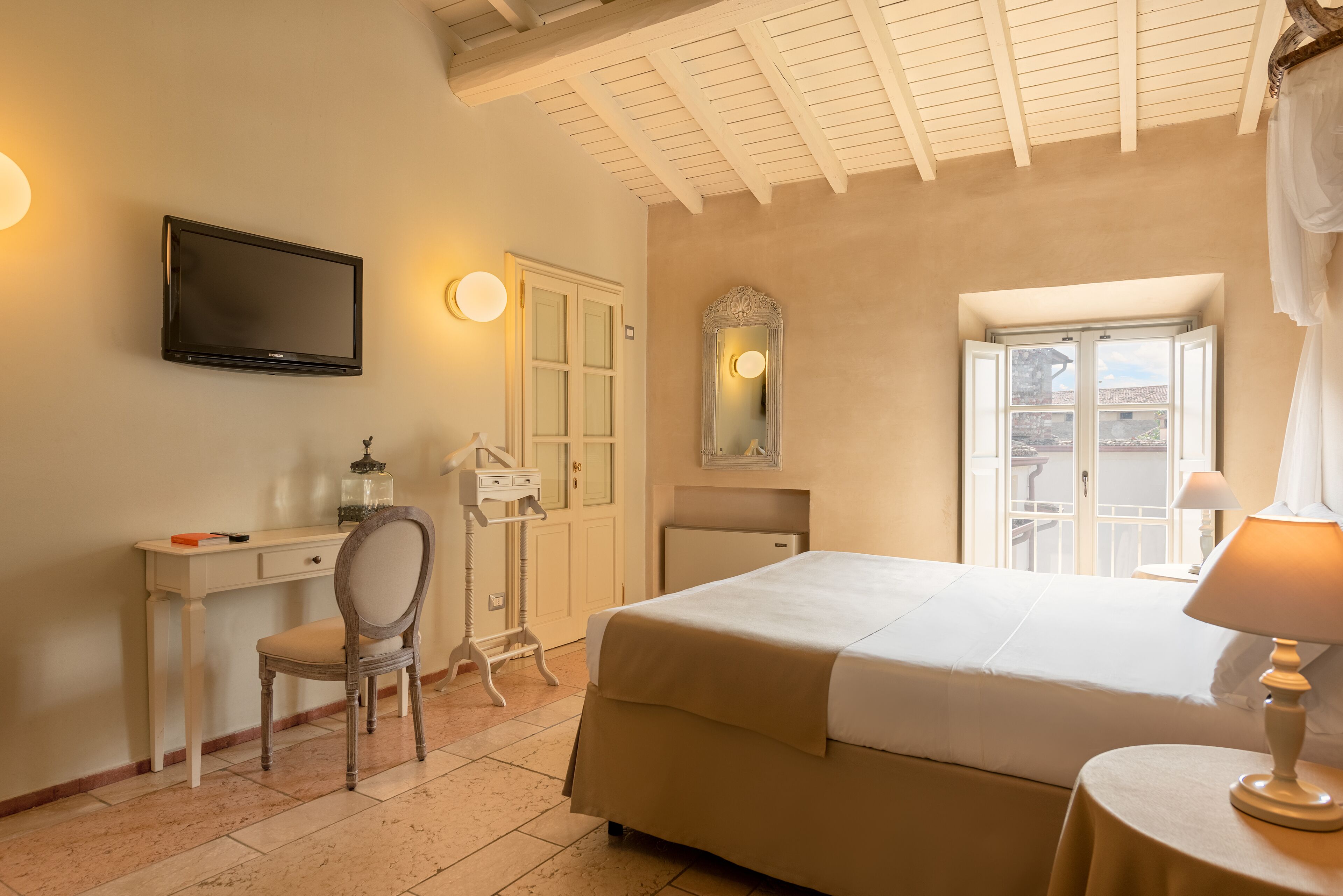 A hotel room with a bed, desk, chair, TV, and a window with a view.
