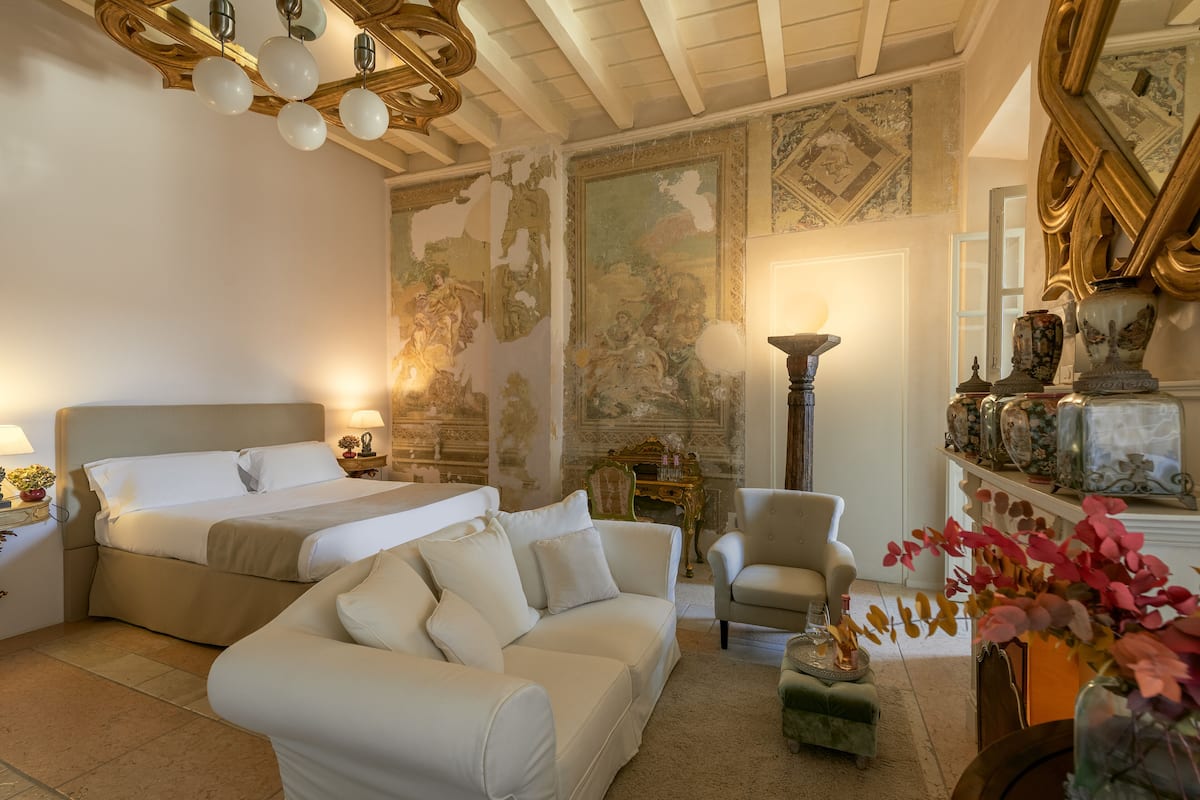 A bedroom with a large bed, a sofa, a chair, and a small table with a lamp.