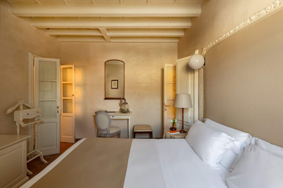A bedroom with a bed, a desk, a chair, a small table, and a mirror.