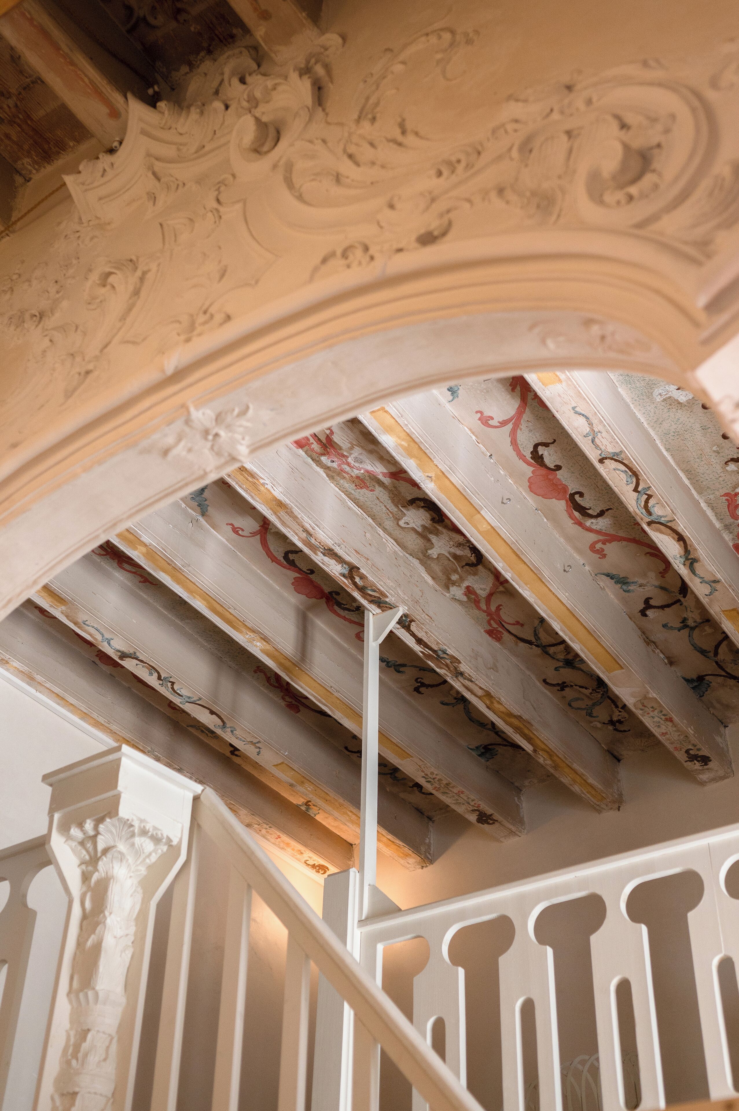 Un escalier orné de rampes blanches et un plafond décoré de motifs floraux complexes.