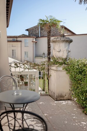 Un balcon avec une table et des chaises, un bac à fleurs décoratif en pierre et une vue sur un bâtiment dont le toit est recouvert de tuiles.