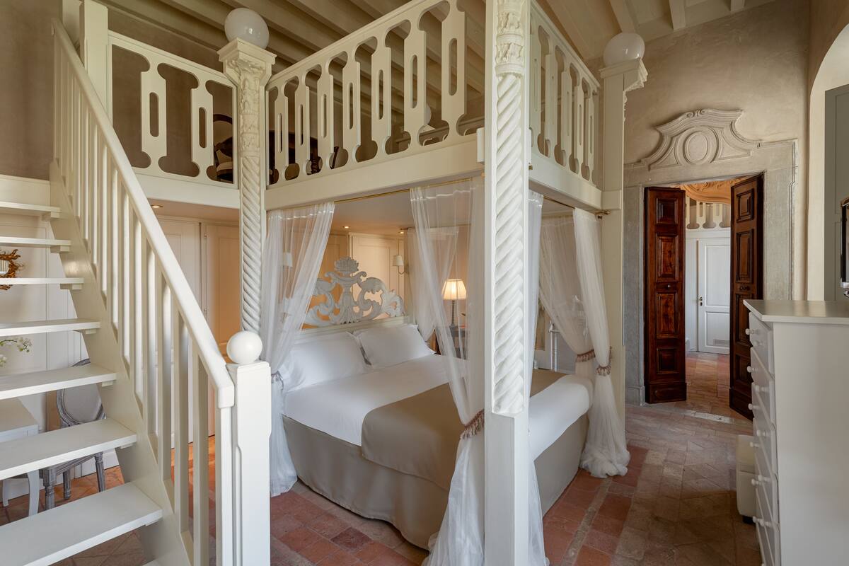 A bedroom with a four-poster bed, a staircase, and a hallway leading to a door.