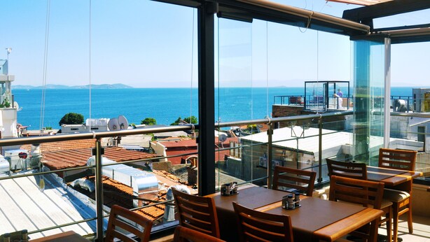 Un restaurante con terraza y vistas al mar, con amplios ventanales y mobiliario de madera.