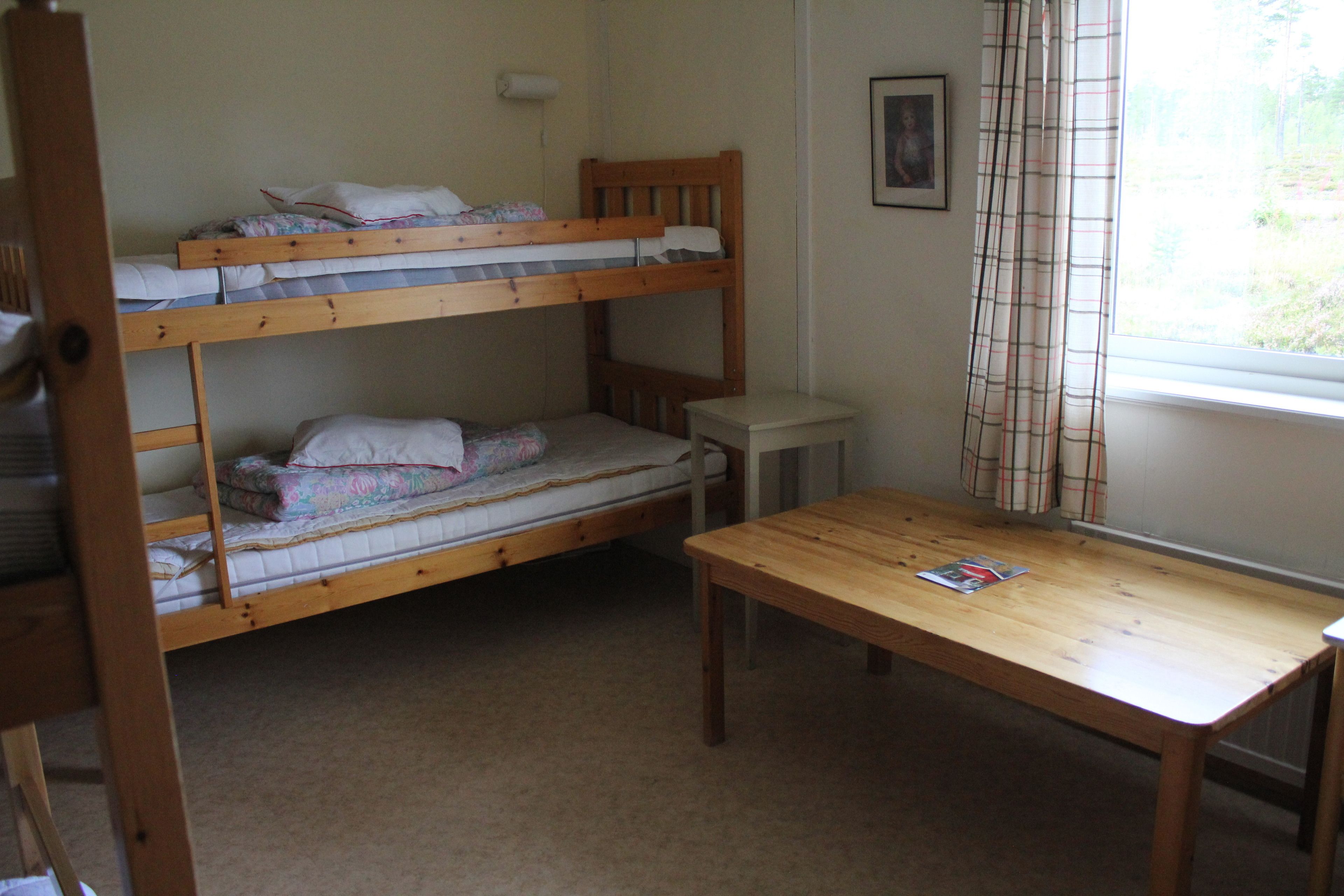 A bunk bed room with a wooden table and a window with curtains.