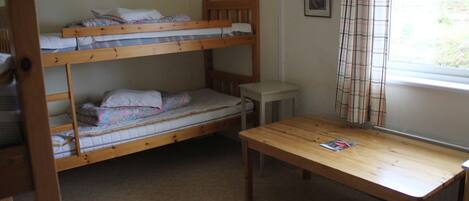 A bunk bed room with a wooden table and a window with curtains.