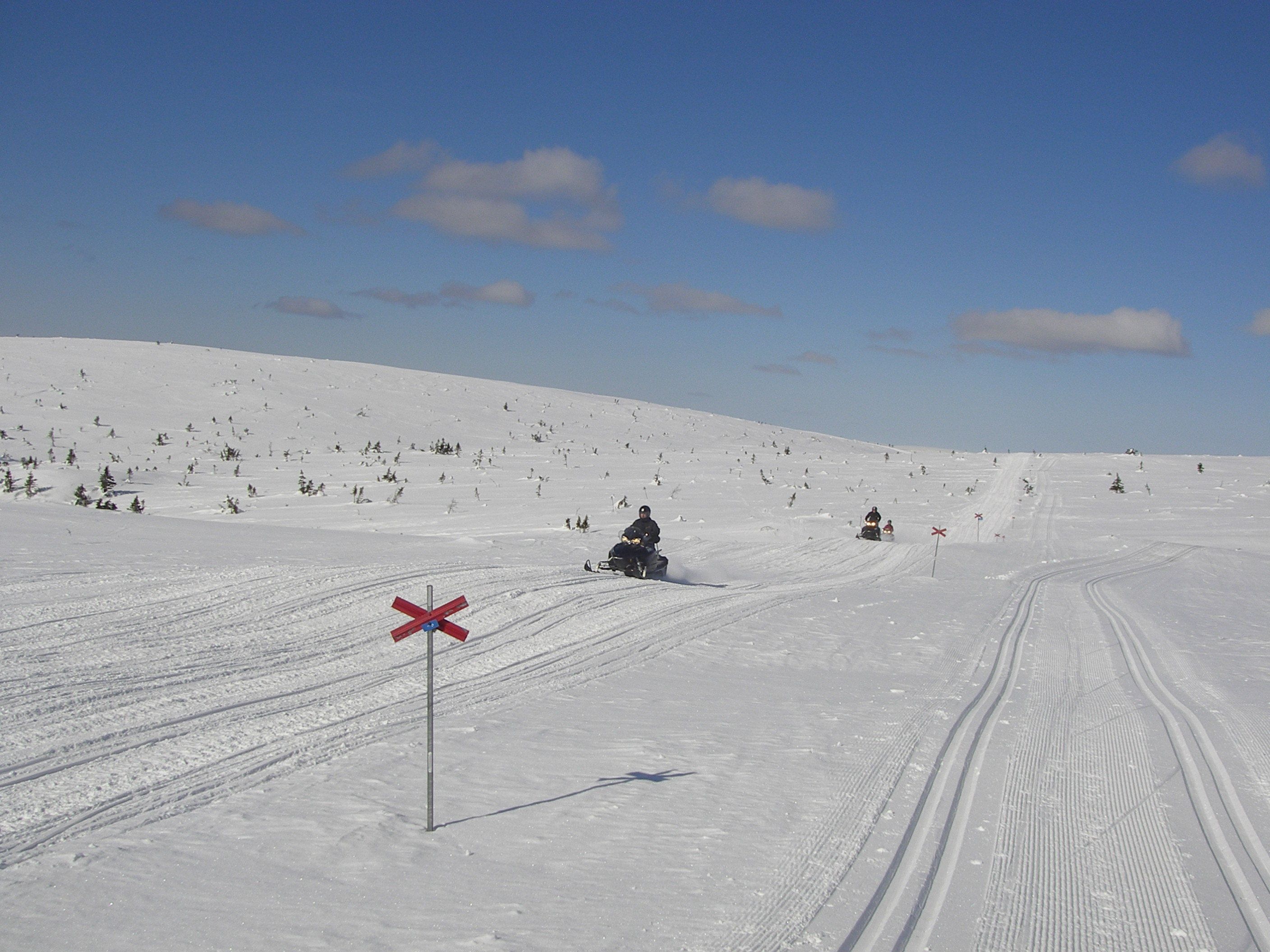 A snowy ski slope with a red cross sign indicating no skiing.