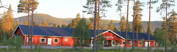 Um edifício vermelho com uma placa que diz "Vandrarhem" em uma área arborizada, com árvores altas e uma montanha ao fundo.