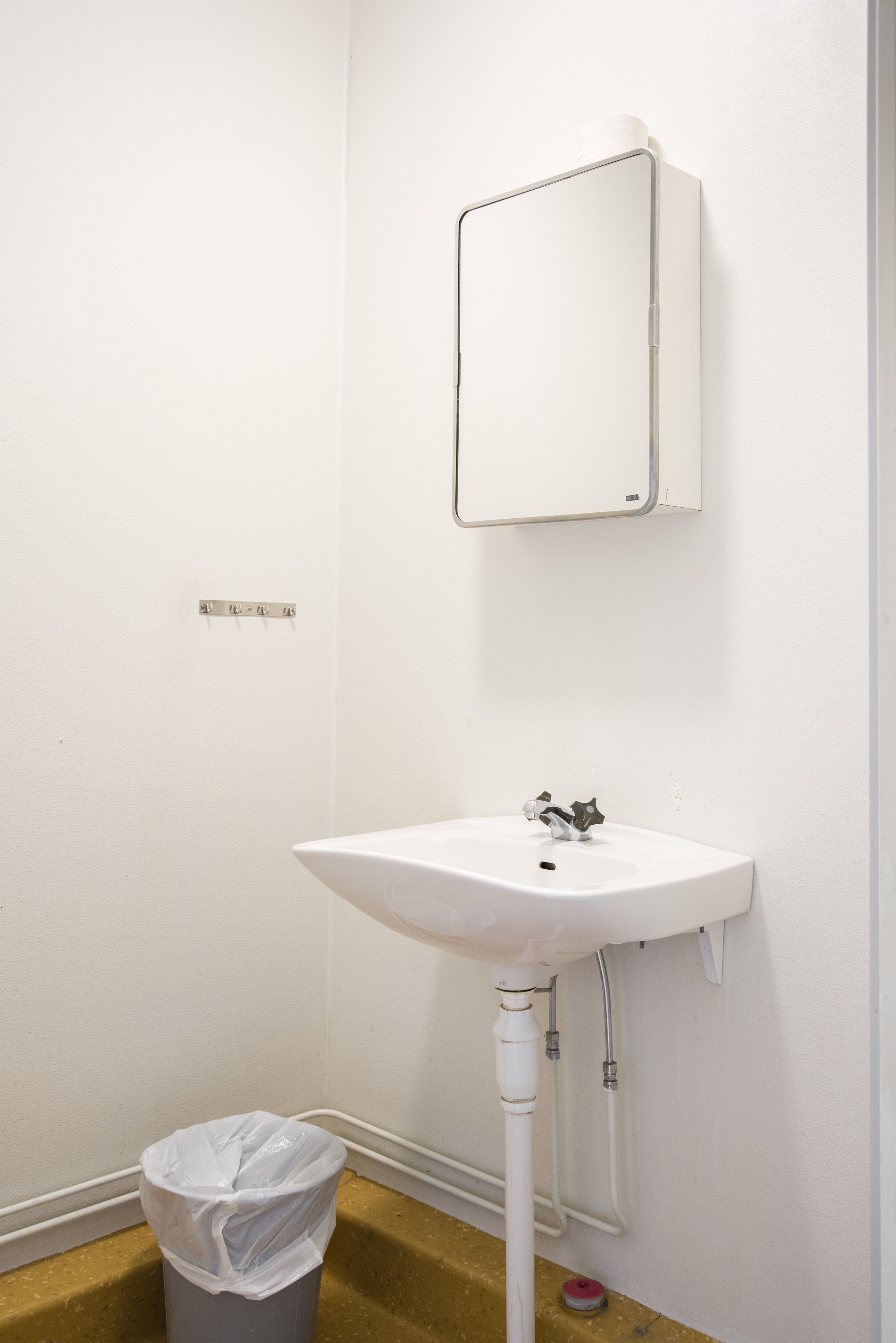A white bathroom with a sink, a mirror, and a trash can.