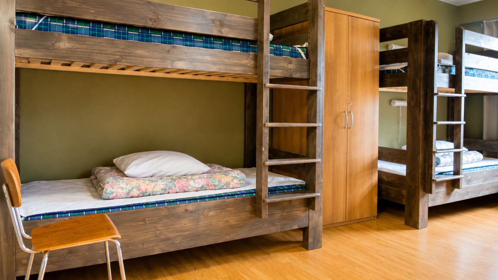 A bunk bed room with a wooden ladder, a wooden chair, and a wardrobe.