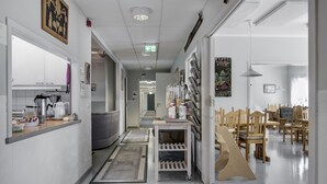 Een gang met een keuken aan de linkerkant, een zithoek met houten stoelen, en een verzameling ingekaderde foto's aan de rechterkant.